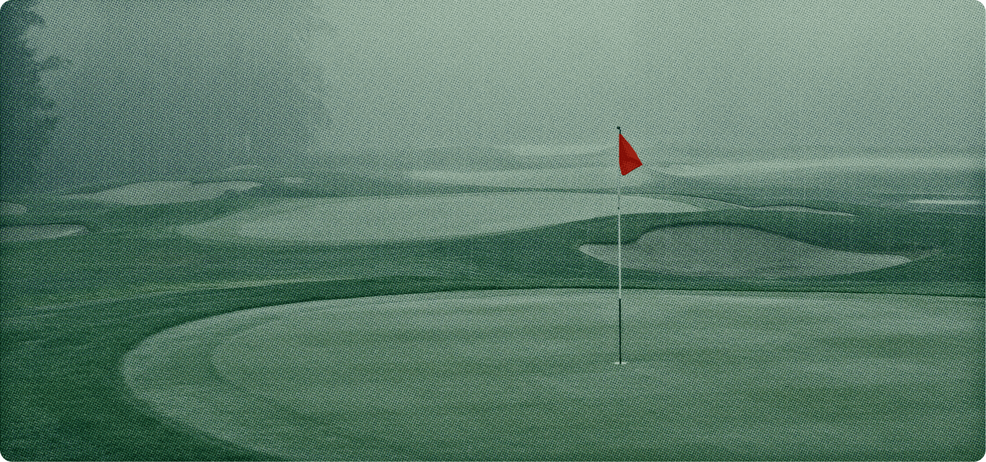 Golf course green at dusk with a red pin flag and fog rolling through the trees