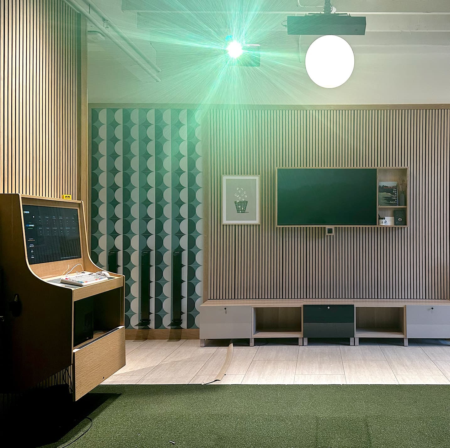 A simulator bay with an Uneekor launch monitor, green laser dot on the wall, and a turf hitting area